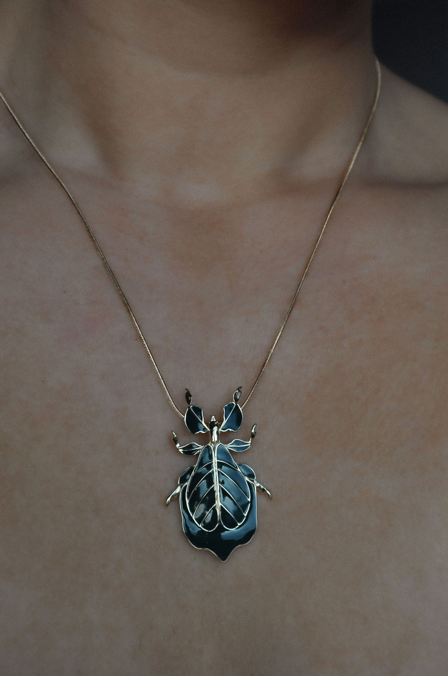Deep green enamel Phylliidae leaf insect pendant worn as a necklace, mirror-polished sterling silver miniature sculpture inspired by the walking-leaf insect.