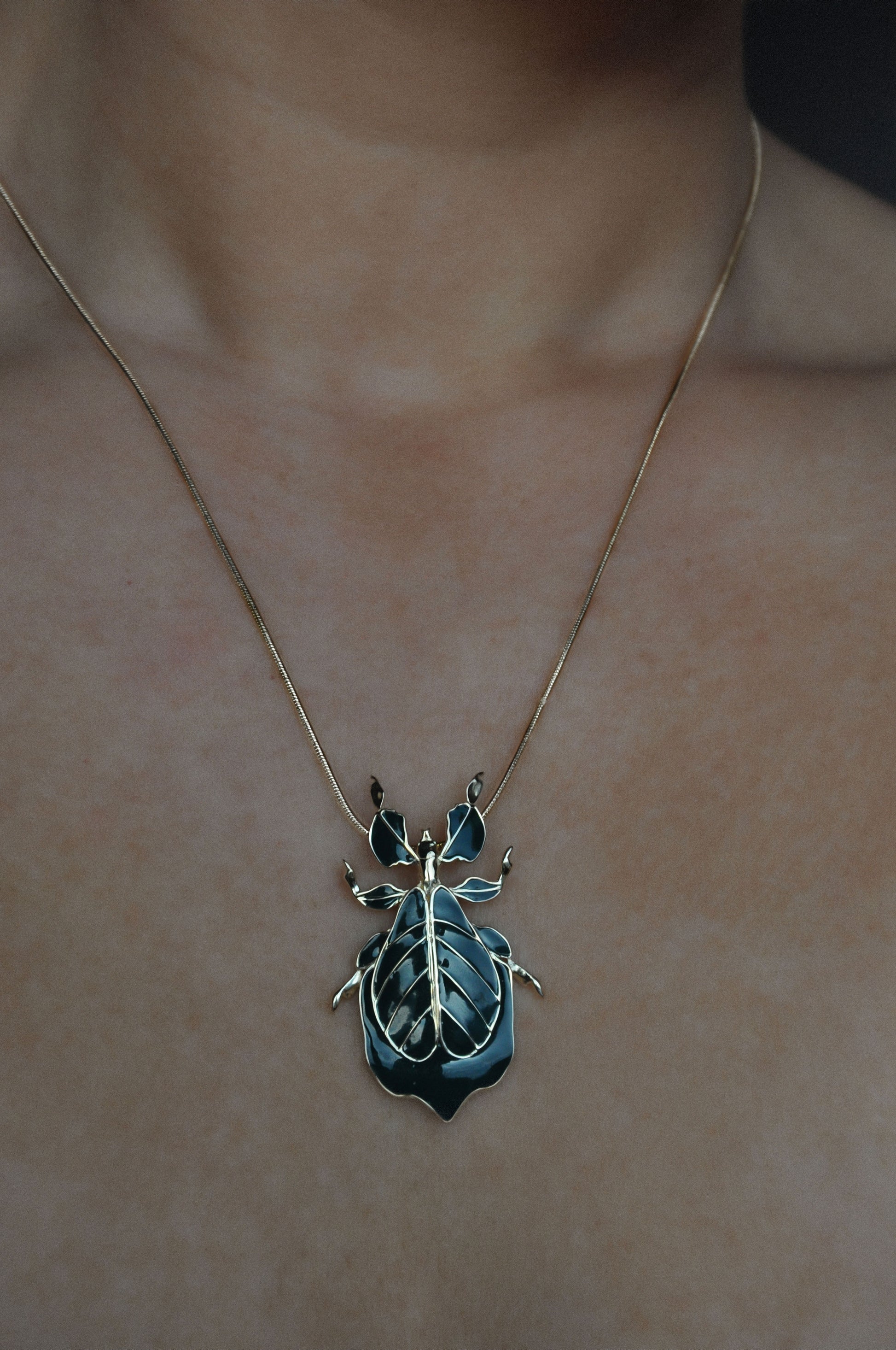 Deep green enamel Phylliidae leaf insect pendant worn as a necklace, mirror-polished sterling silver miniature sculpture inspired by the walking-leaf insect.