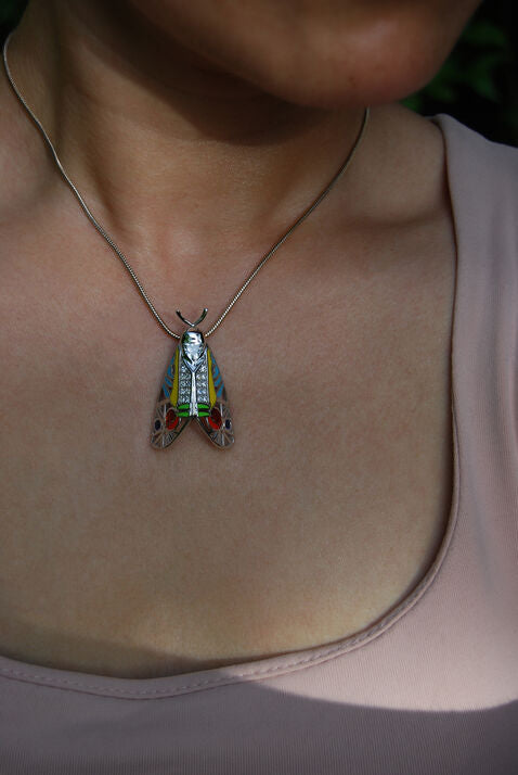 Model wearing Picasso Moth pendant with colorful enamel and zirconia stones, styled as insect jewelry in natural light