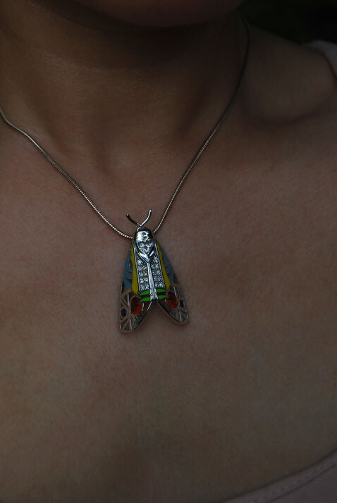 Picasso Moth pendant worn by model outdoors, highlighting colorful enamel, zirconia stones, and sterling silver craftsmanship
