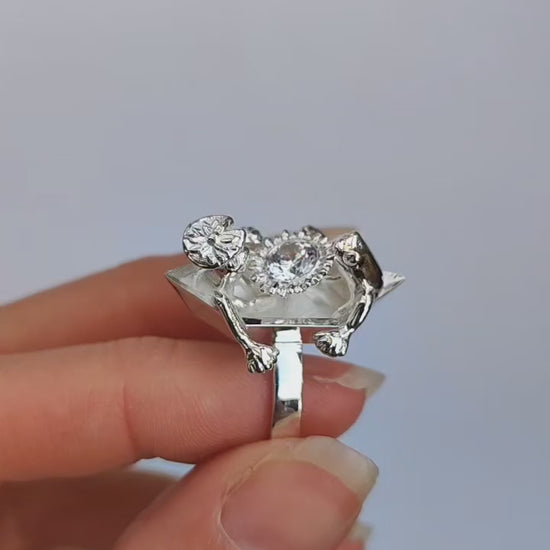 Video showing a sterling silver ring worn on a finger, with two sculpted frogs on a boat‑shaped top holding a clear faceted crystal.