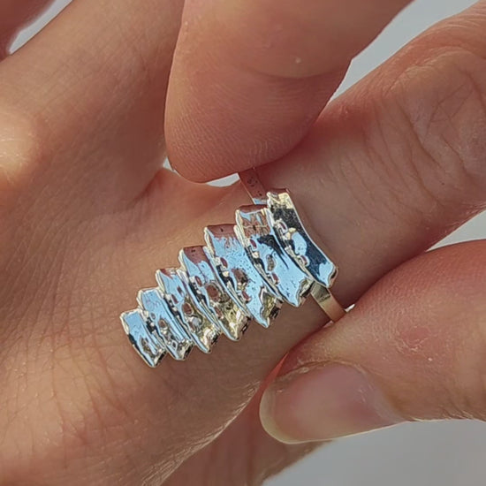Mixed‑metal trilobite beetle stacking rings—silver, gold, and dark‑toned segments—worn together on one finger to show how the sculptural pieces stack and interlock.