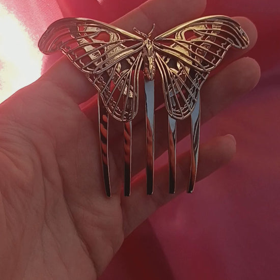 Video showcasing a bronze Atlas Moth hair comb, highlighting its sculptural wing design and warm metallic finish as it catches the light in motion. The comb is styled to evoke elegance and nature-inspired artistry.