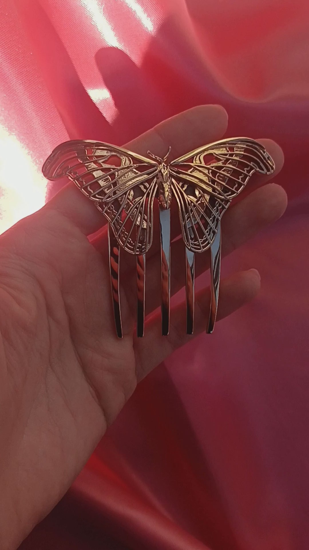Video showcasing a bronze Atlas Moth hair comb, highlighting its sculptural wing design and warm metallic finish as it catches the light in motion. The comb is styled to evoke elegance and nature-inspired artistry.