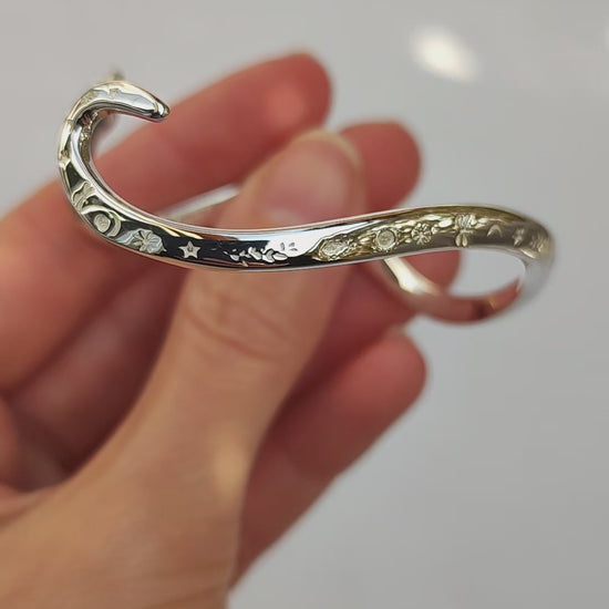 Video showing a sterling silver snake bracelet in motion, highlighting its polished surface, engraved celestial details, and sculptural curves from multiple angles.