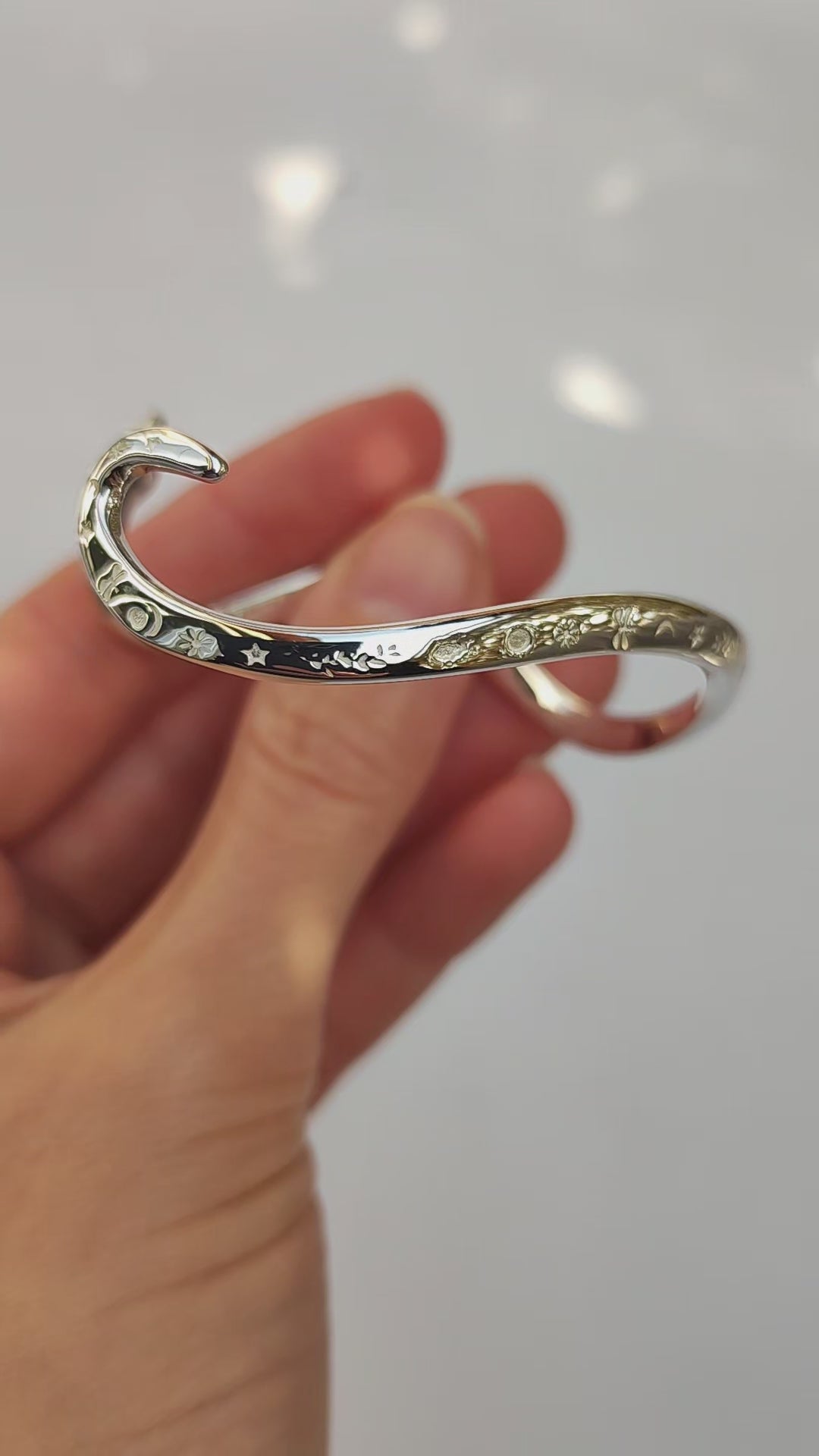 Video showing a sterling silver snake bracelet in motion, highlighting its polished surface, engraved celestial details, and sculptural curves from multiple angles.