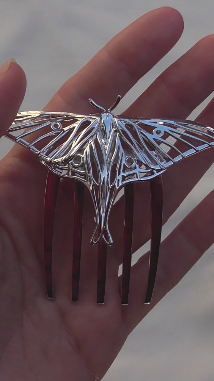 Video showcasing a handcrafted Luna Moth hair comb in rhodium-plated silver finish, displayed on a white background to highlight its intricate wing details and elegant insect-inspired design.