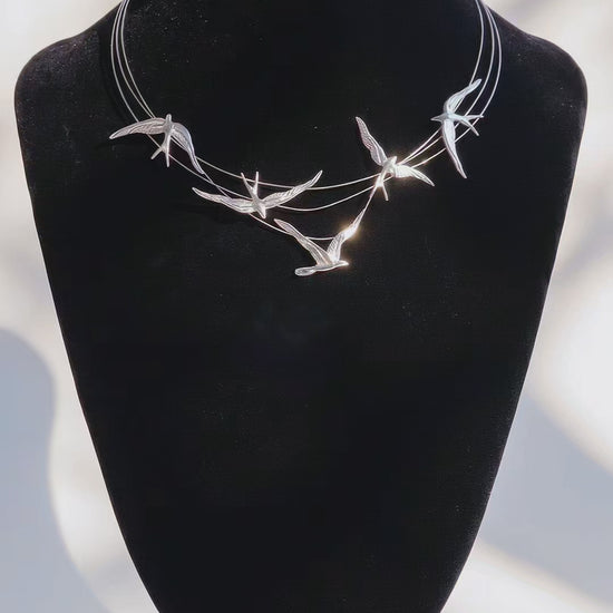 Sterling silver necklace with sculpted swallows in flight along fine arcs, reflecting light on a black velvet bust.