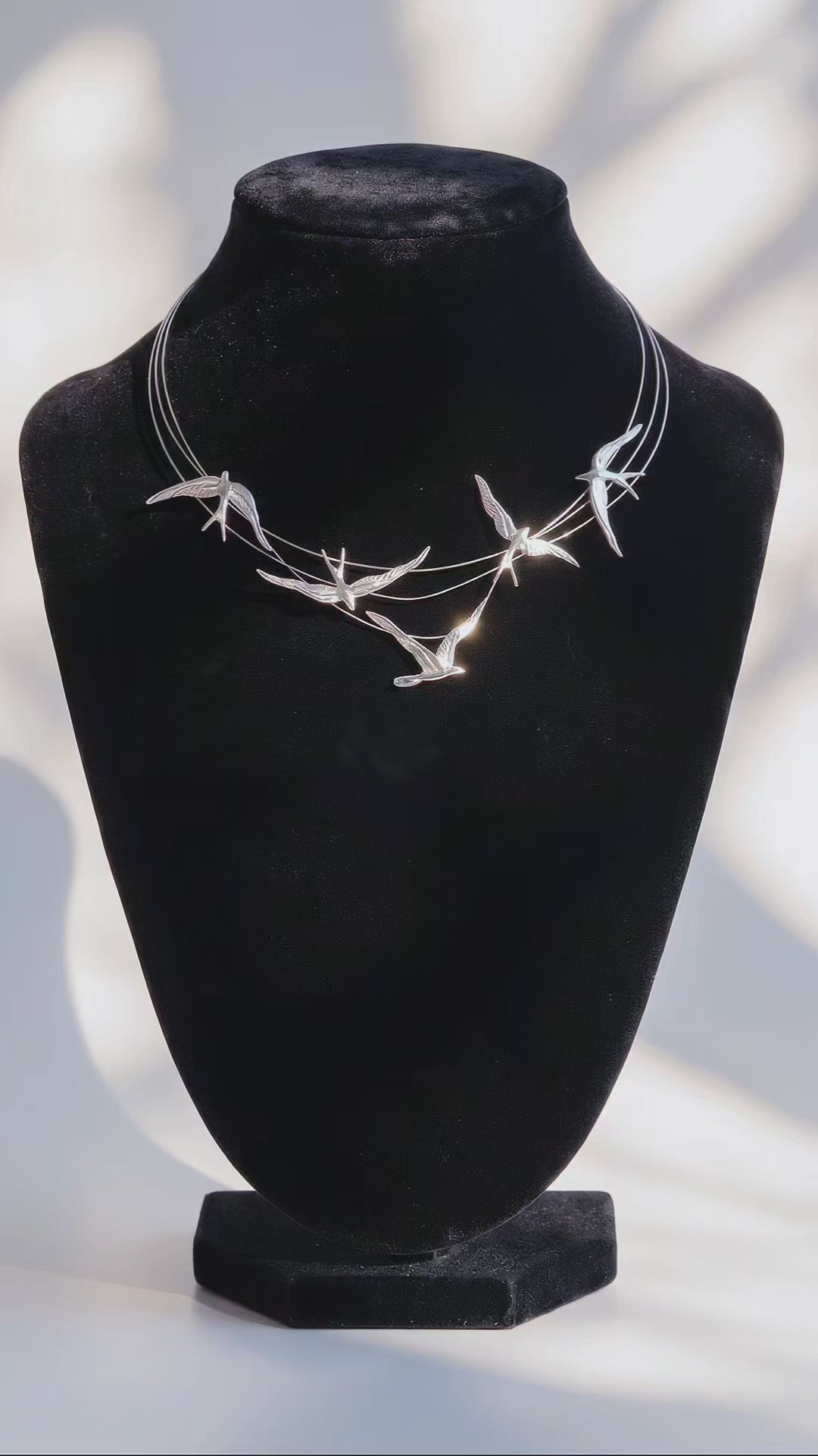 Sterling silver necklace with sculpted swallows in flight along fine arcs, reflecting light on a black velvet bust.