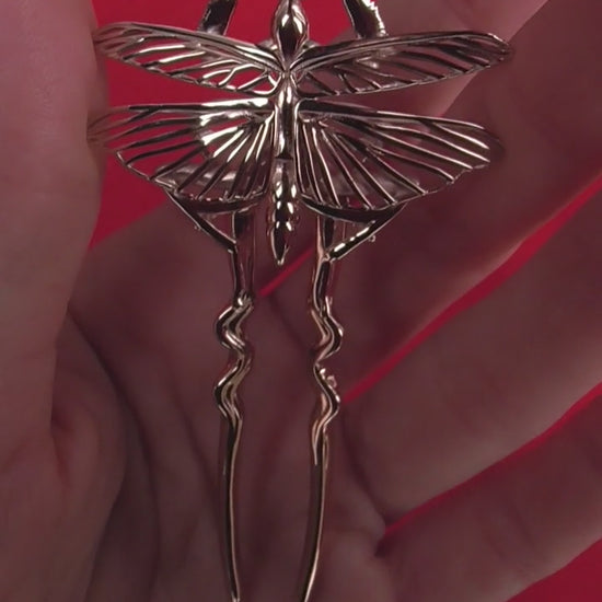 Video showing Orchid Mantis hairpins held in hand against red background, delicate and sharp with metallic sheen.