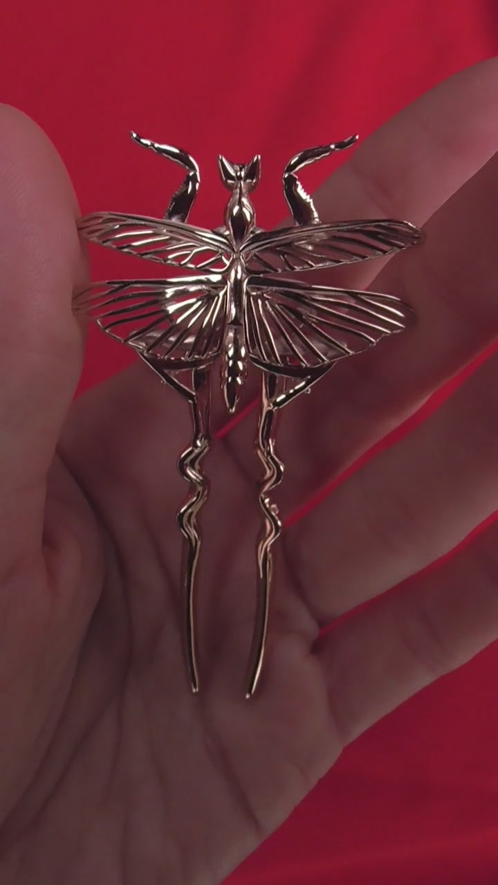 Video showing Orchid Mantis hairpins held in hand against red background, delicate and sharp with metallic sheen.
