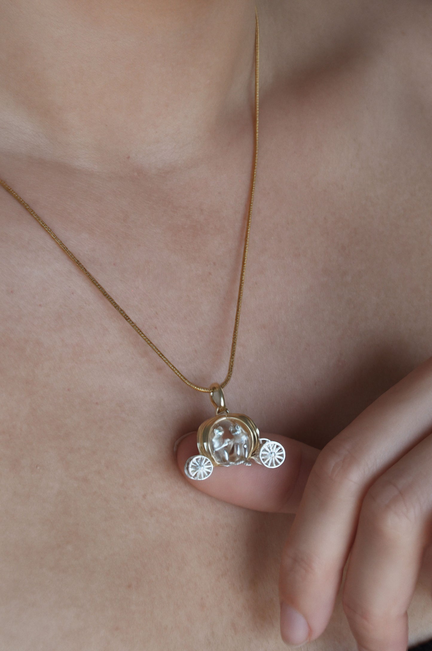 Frogs in Pumpkin Carriage Pendant worn on a necklace, showing a gold pumpkin carriage with miniature sculptural passengers.