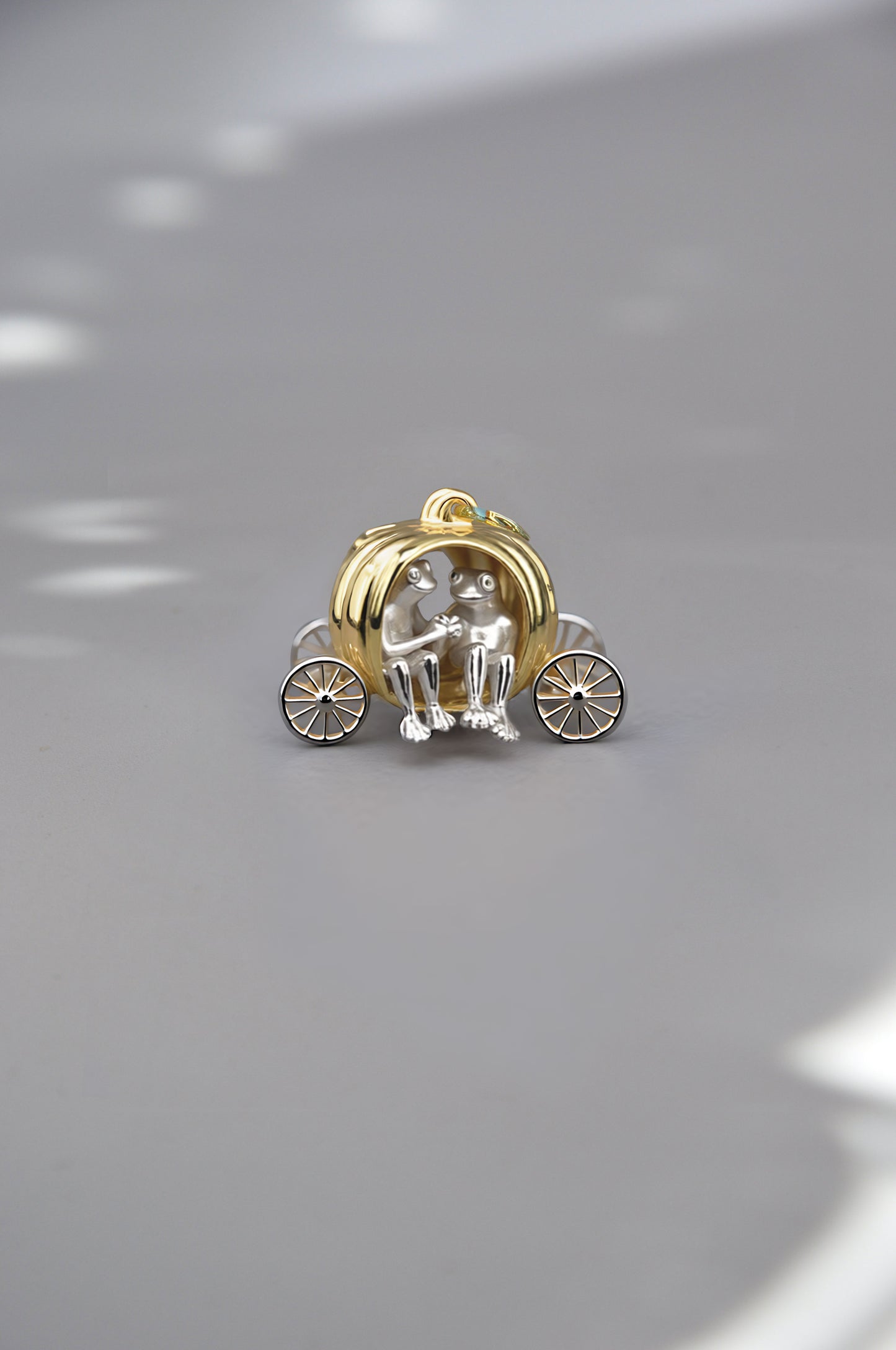 Miniature pumpkin carriage pendant in gold with two tiny sculptural figures inside, crafted as a whimsical fairy‑tale collectible.