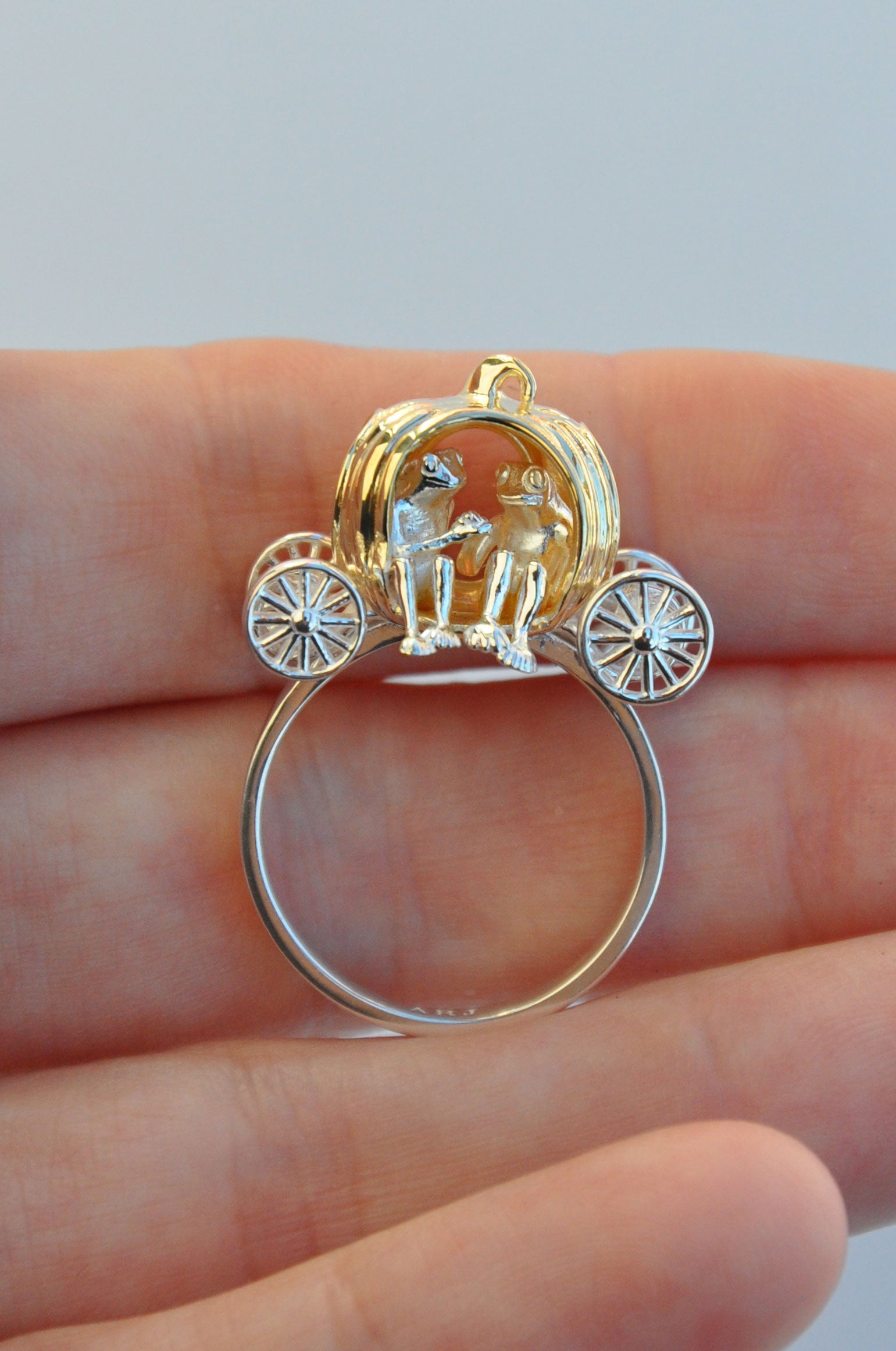Miniature pumpkin carriage ring held between fingers, showcasing a gold carriage with sculptural interior details and freely spinning wheels.