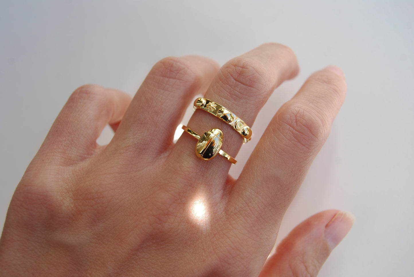 Close-up of celestial scarab stacking rings on finger, highlighting intricate scarab and moon phase details in polished gold.
