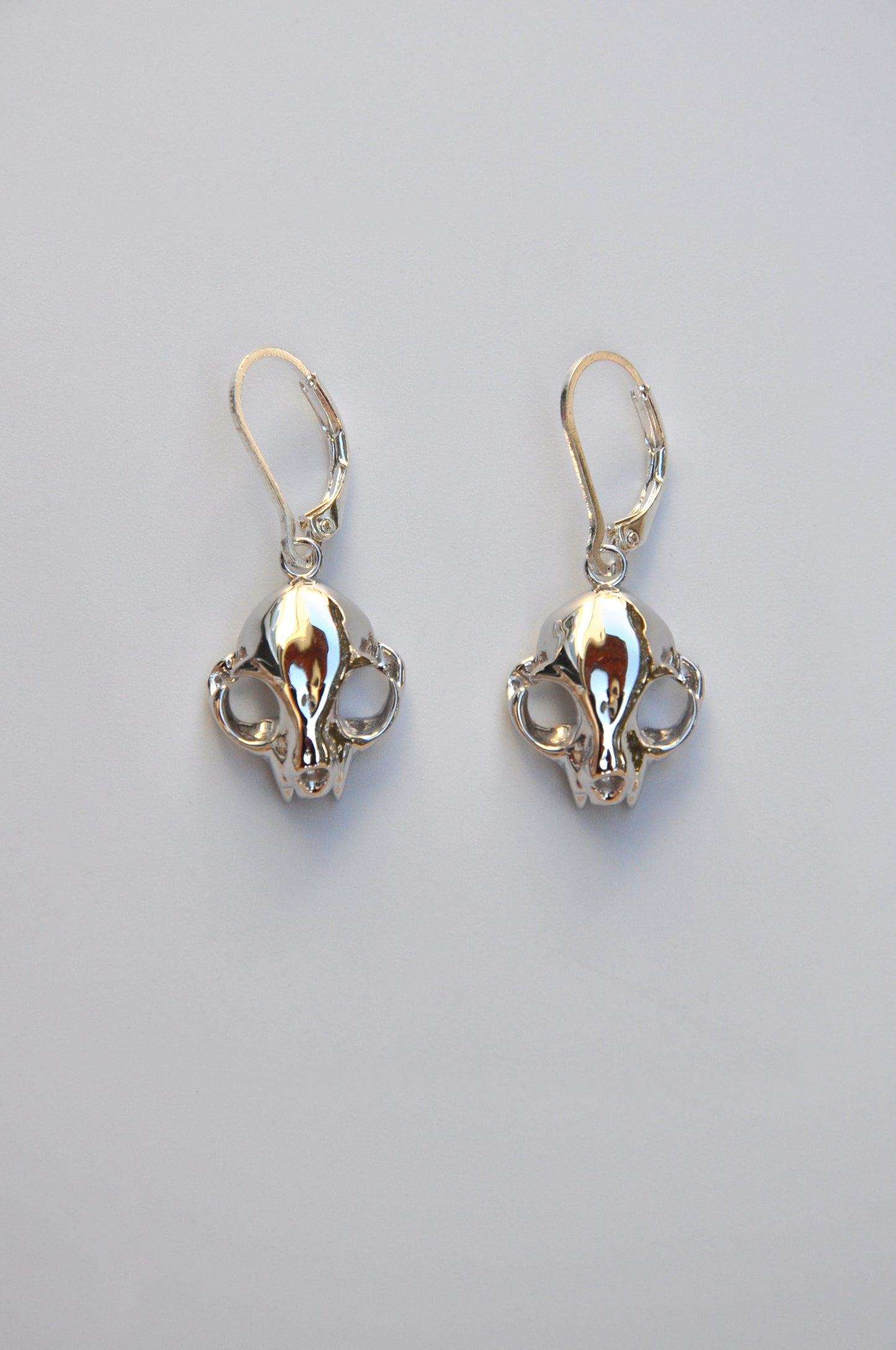 Silver feline skull dangle drop earrings displayed on a white background, showing detailed craftsmanship.