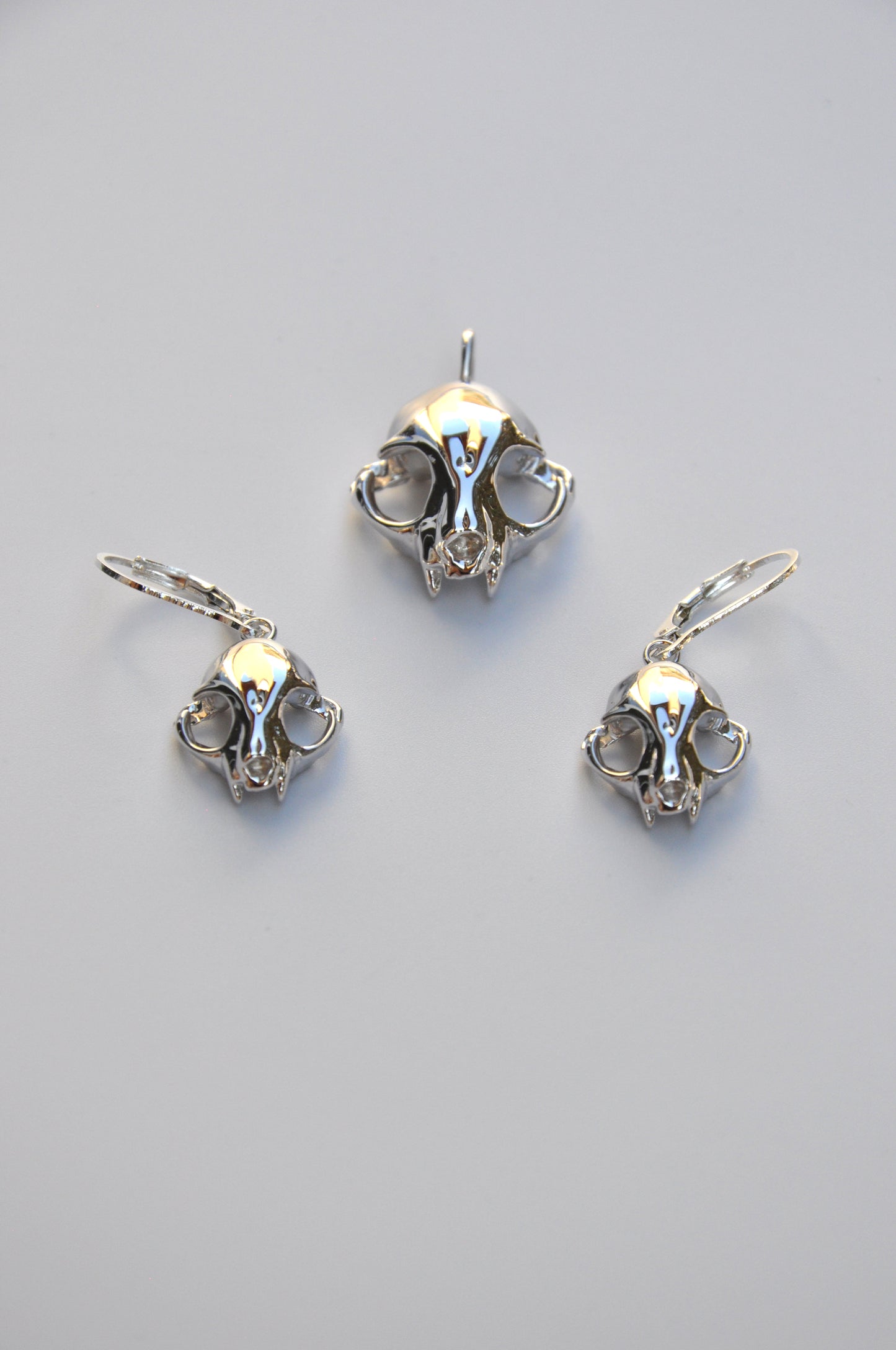 Silver feline skull drop earrings paired with matching pendant on a white background, highlighting the coordinated set.