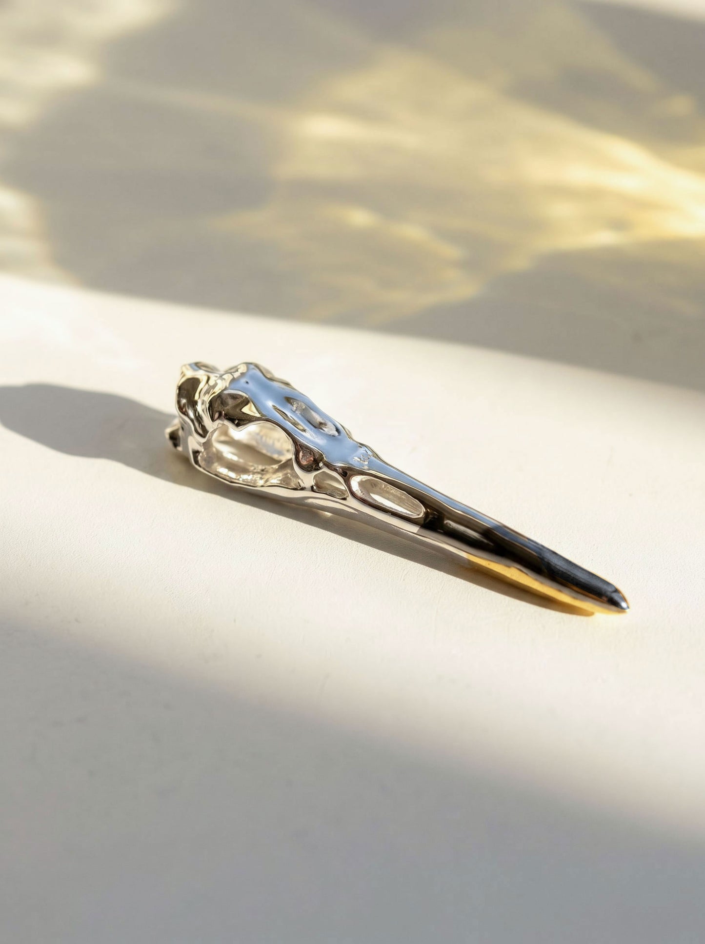 Close-up of Silver Heron Skull Pendant on light surface, showing polished sterling silver skull with elongated beak and finely engraved anatomical details.