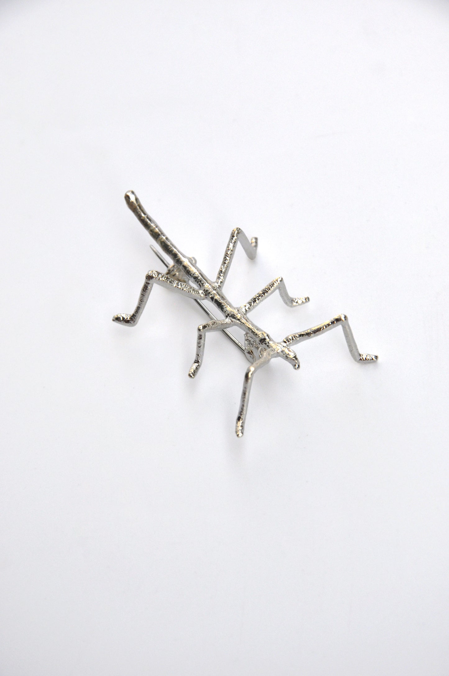 Angled view of the silver stick insect brooch on white background, highlighting the delicate craftsmanship.