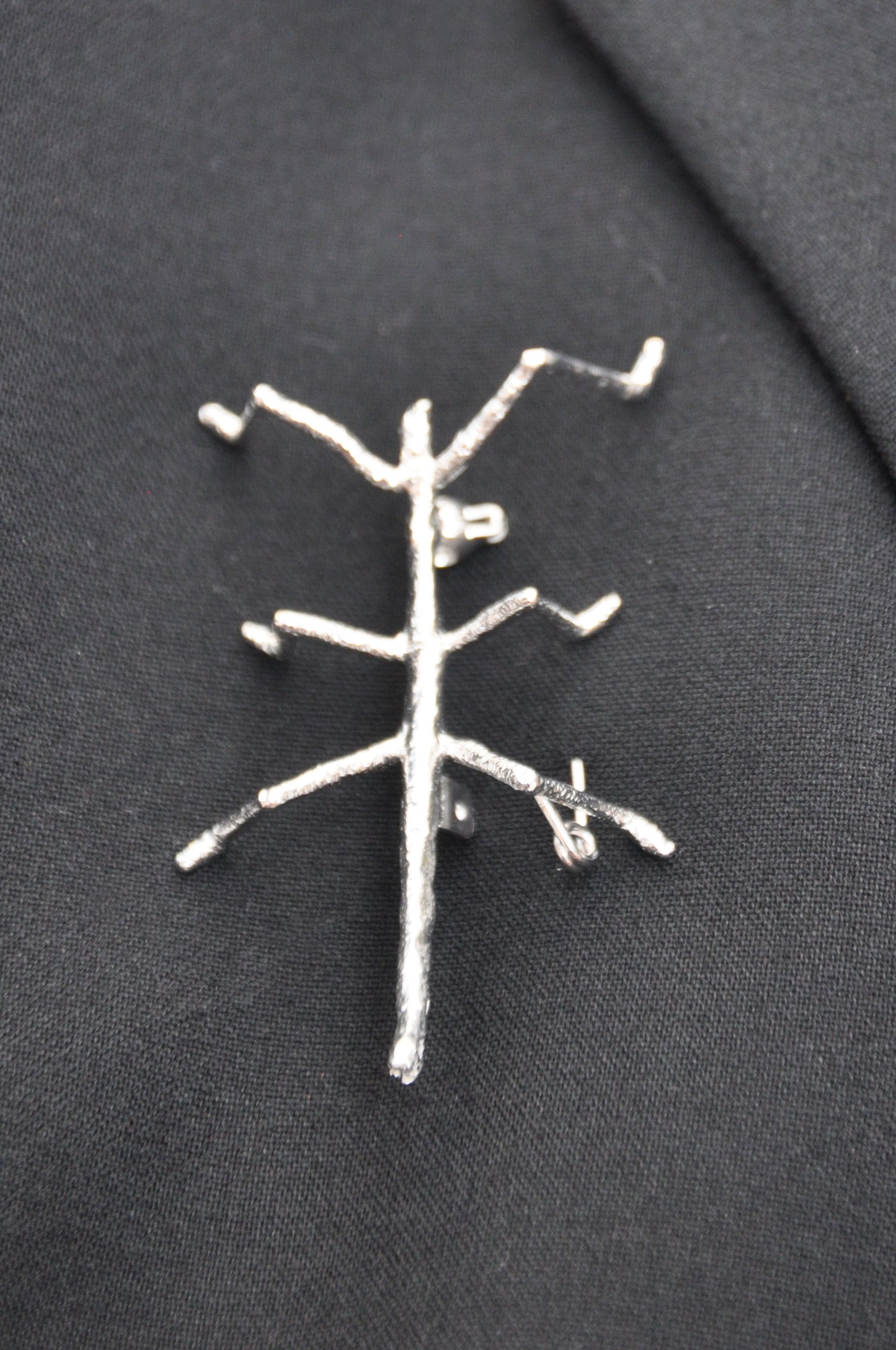 Silver stick insect brooch pinned on dark cloth, highlighting its refined shine and contrast against the fabric