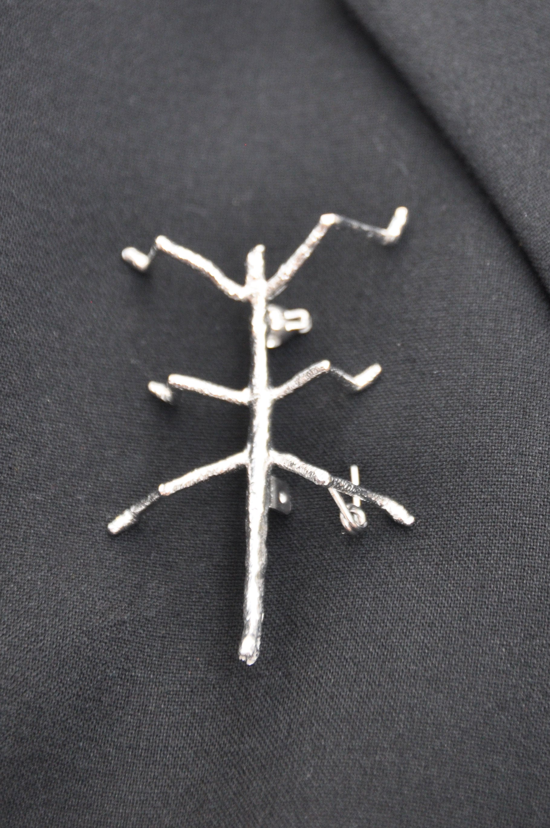 Silver stick insect brooch pinned on dark cloth, highlighting its refined shine and contrast against the fabric