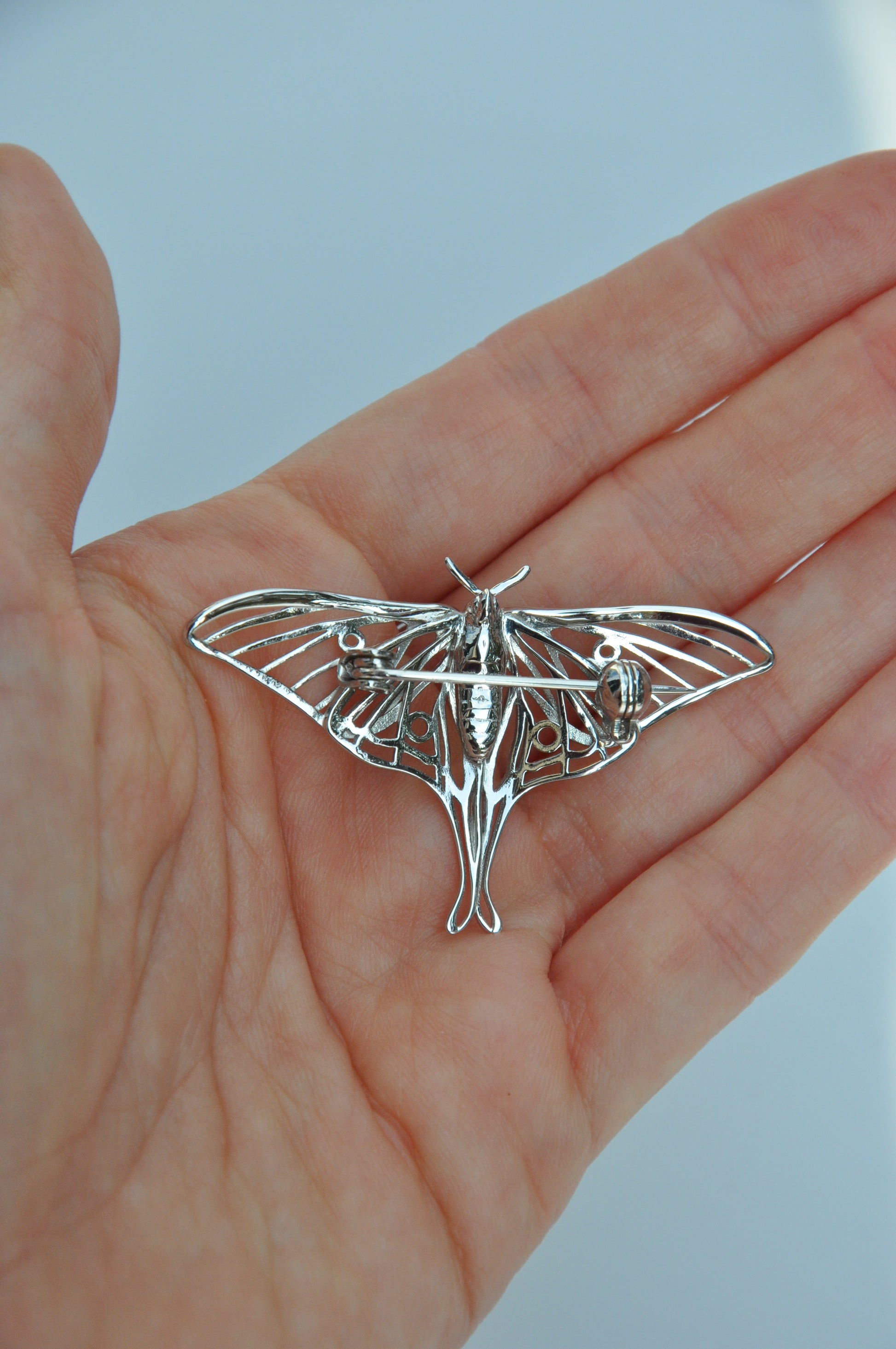 Back view of the silver Luna Moth brooch on a hand, showing the secure pin clasp and polished details.