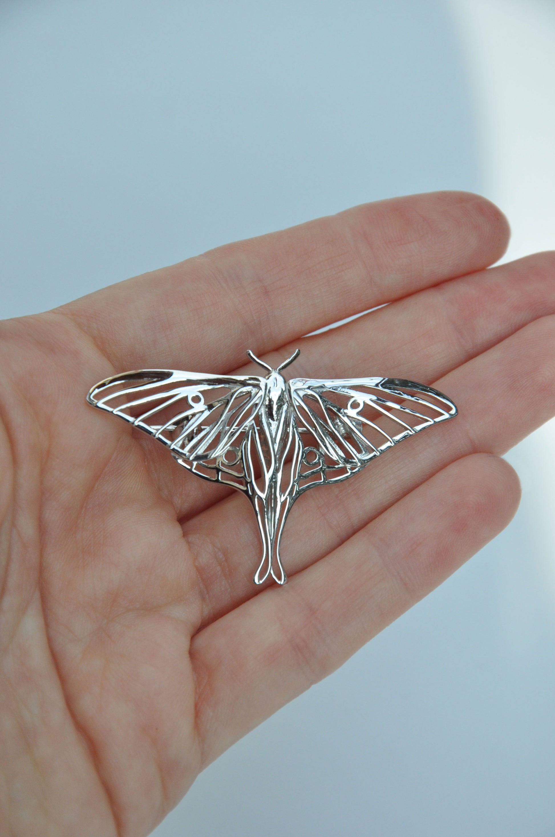 Front view of the silver Luna Moth brooch worn on a hand, displaying its size and intricate design.