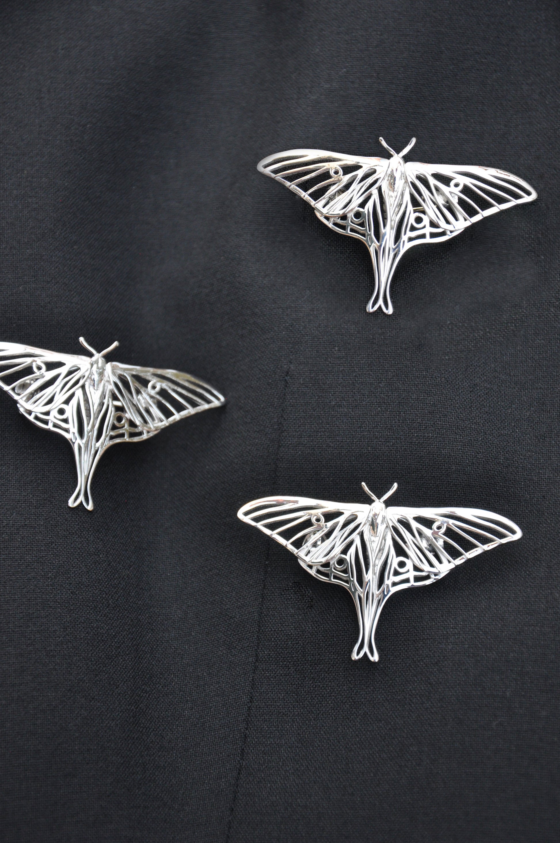  Silver Luna Moth brooch pinned on black cloth, emphasizing its shine and elegant insect-inspired design.