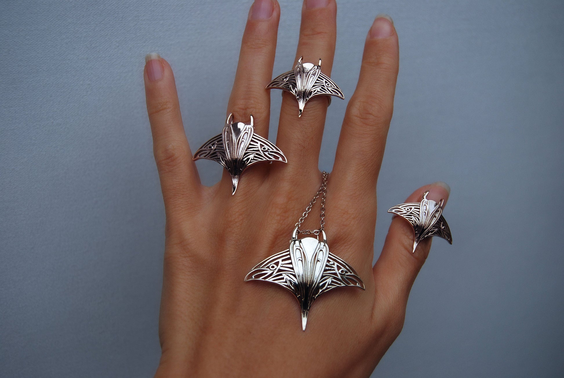 Side view of sterling silver manta ray ring and pendant on hand, showcasing intricate marine details.