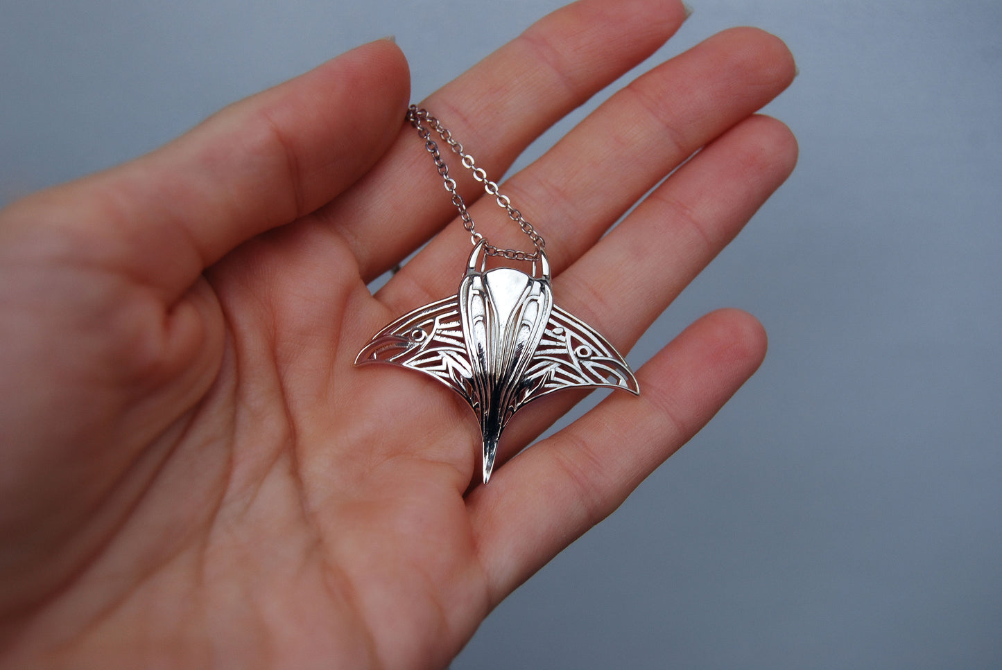 Sterling silver manta ray pendant displayed on hand, showcasing intricate wing cut-outs
