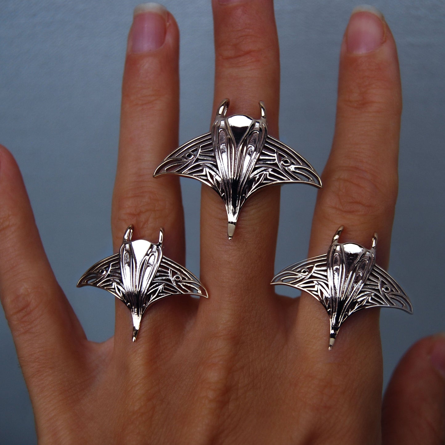 Hand wearing large and small sterling silver manta ray rings, showcasing ocean-inspired jewelry.