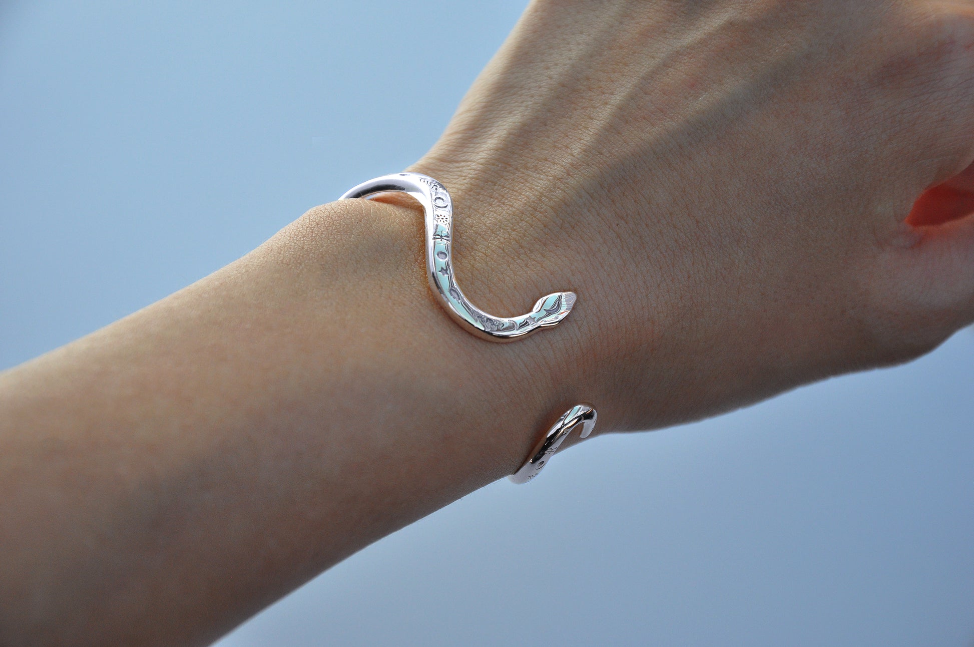 Sterling silver snake bracelet and rings worn on the hand against a grey background, showing sculptural curves and polished details.