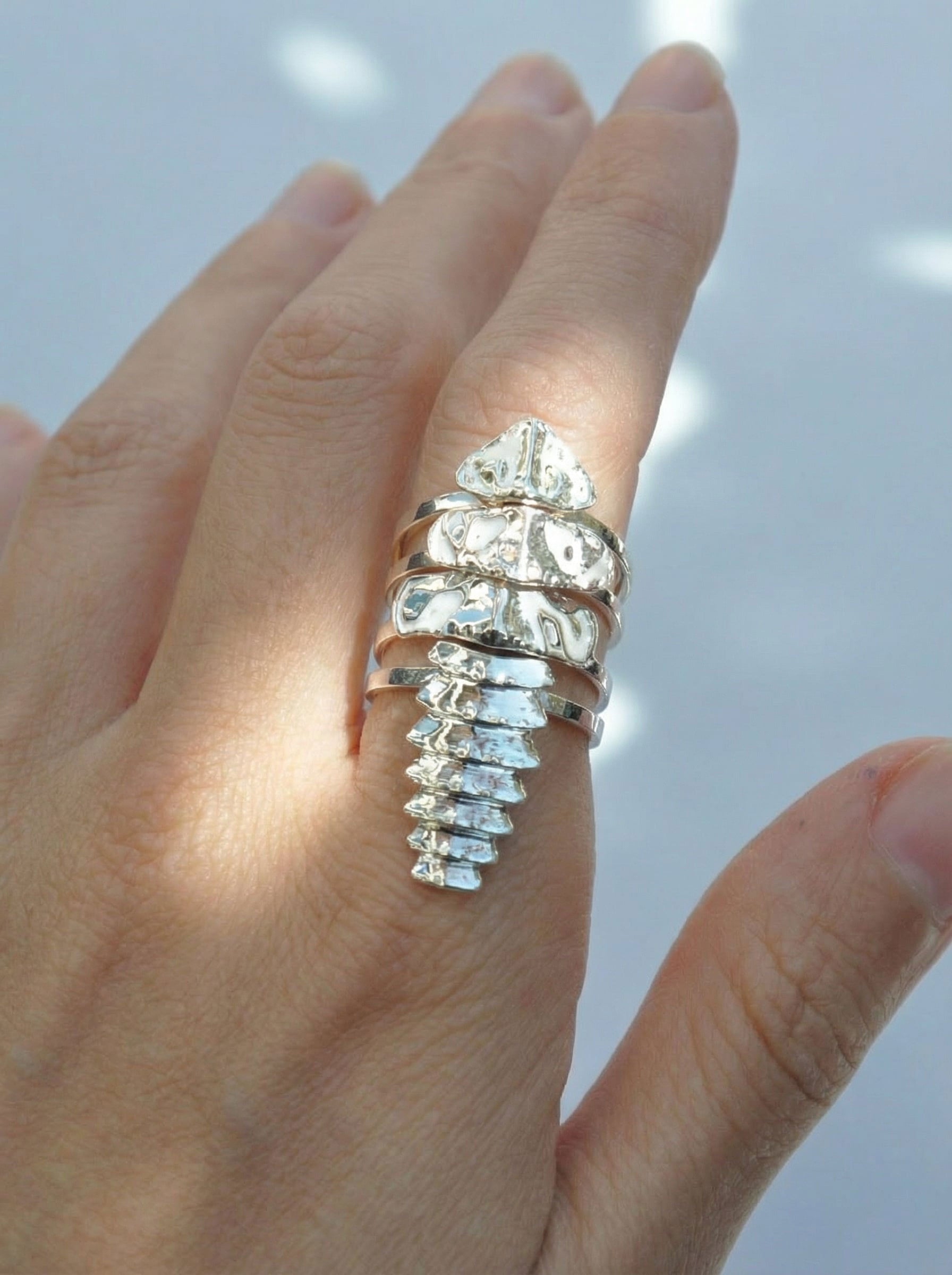 Close‑up of a hand wearing a silver trilobite beetle stacking ring set, with segmented bands forming a sleek, continuous structure.
