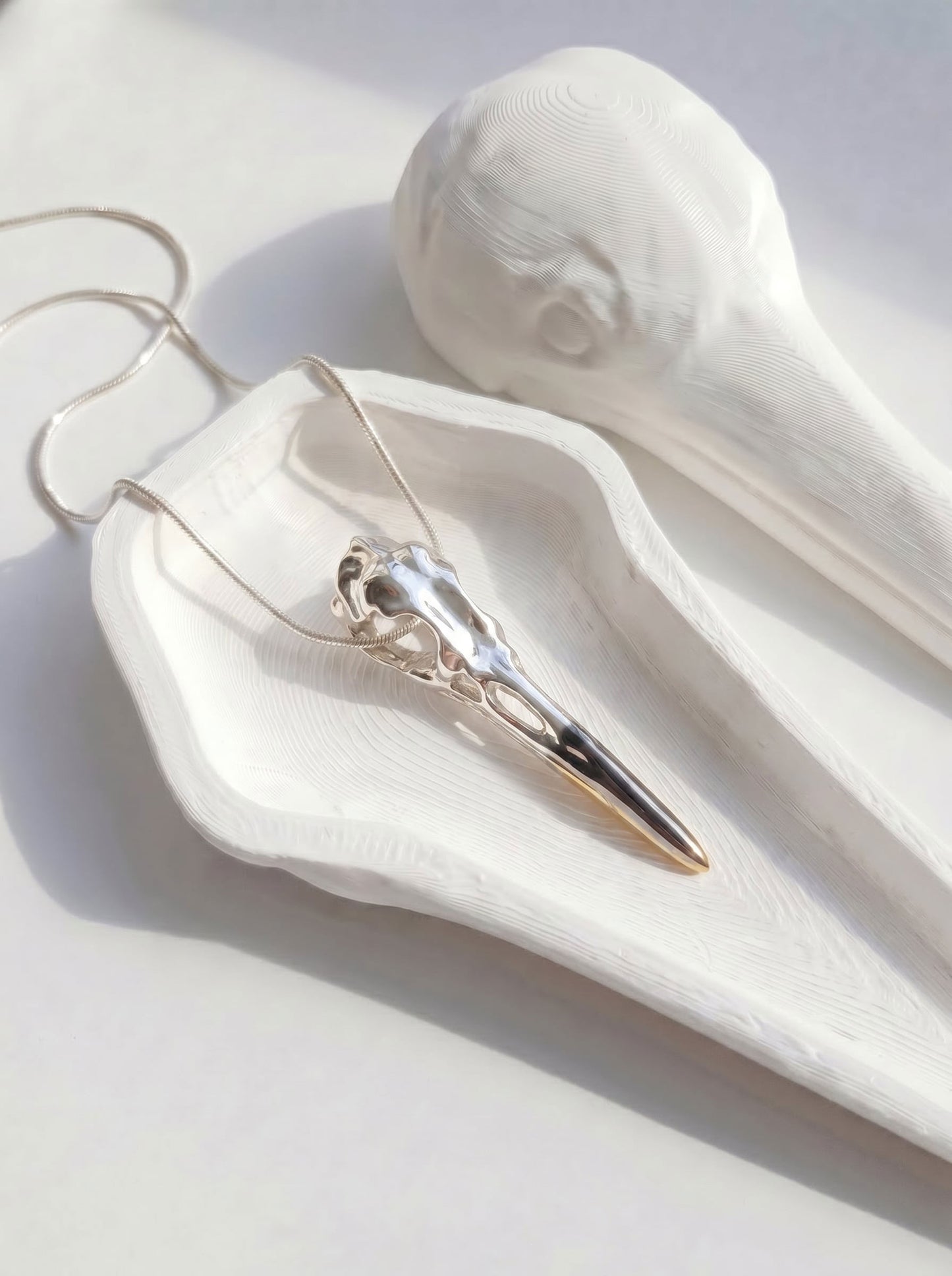 Silver Heron Skull Pendant displayed on white tray, showing clean lines and interplay of silver, rhodium, and gold tones.
