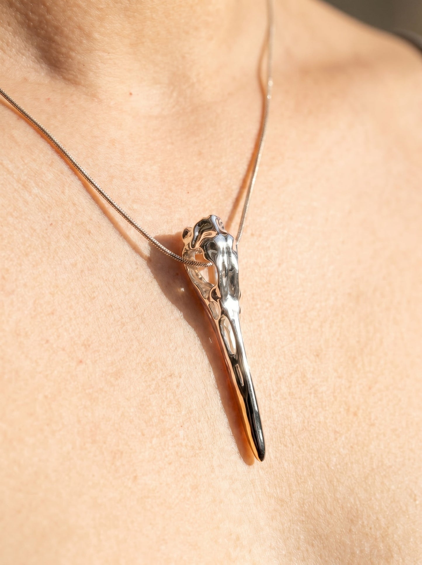 Silver Heron Skull Pendant worn on neck, highlighting elongated sculptural silhouette and mixed‑metal gradient from rhodium to gold.