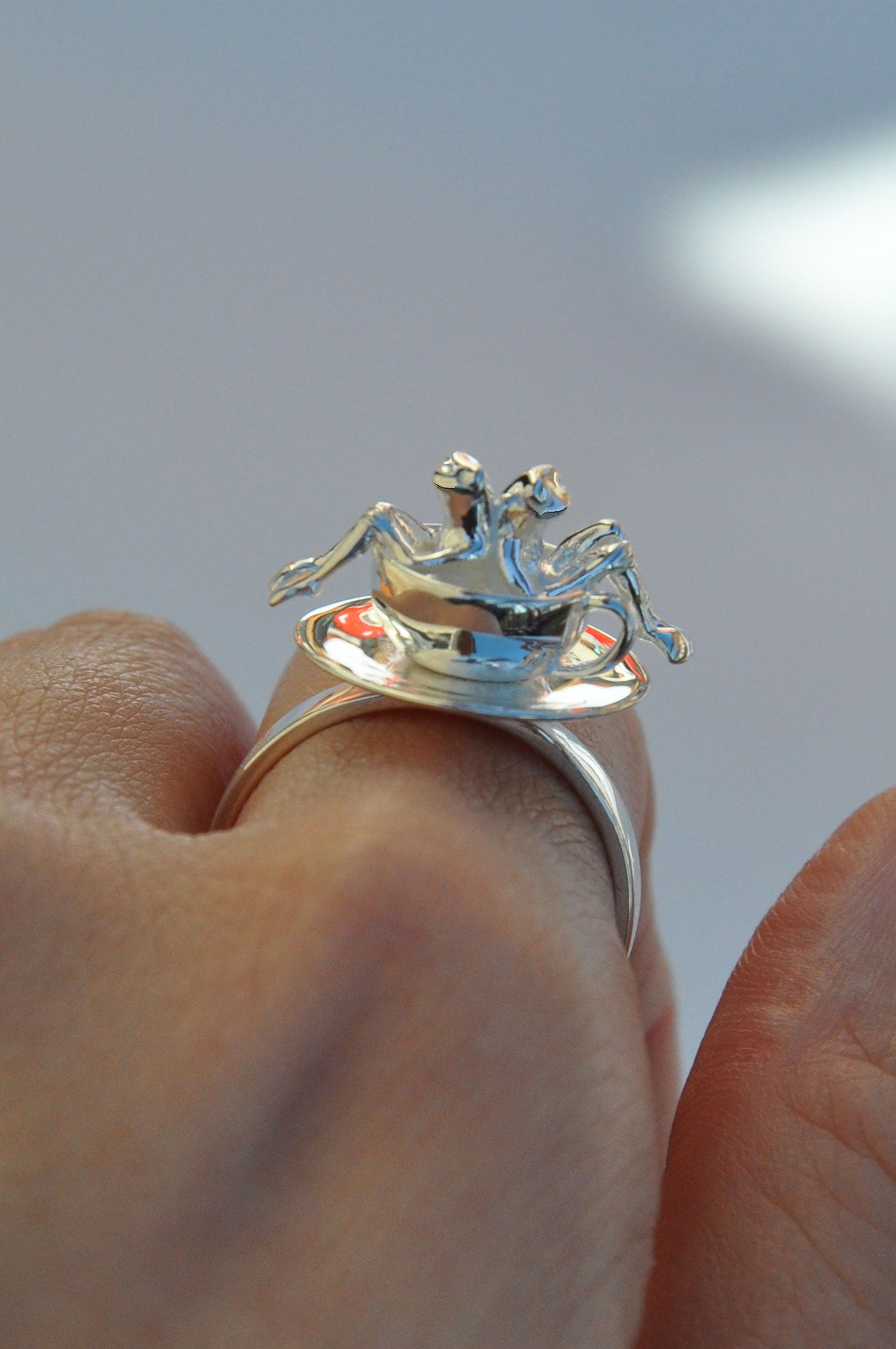 Spinning Teacup Frogs Carousel Ring worn on a finger, showing two miniature frogs riding inside a rotating silver teacup.