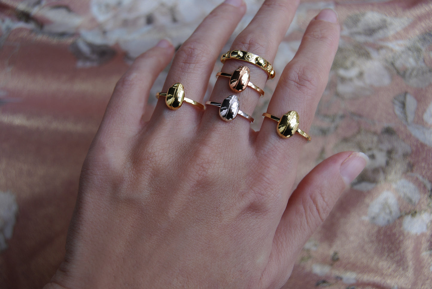 Multiple celestial scarab rings stacked on hand in 14K gold plated, 14K rose gold, and sterling silver, highlighting mixed metal insect jewelry styling.