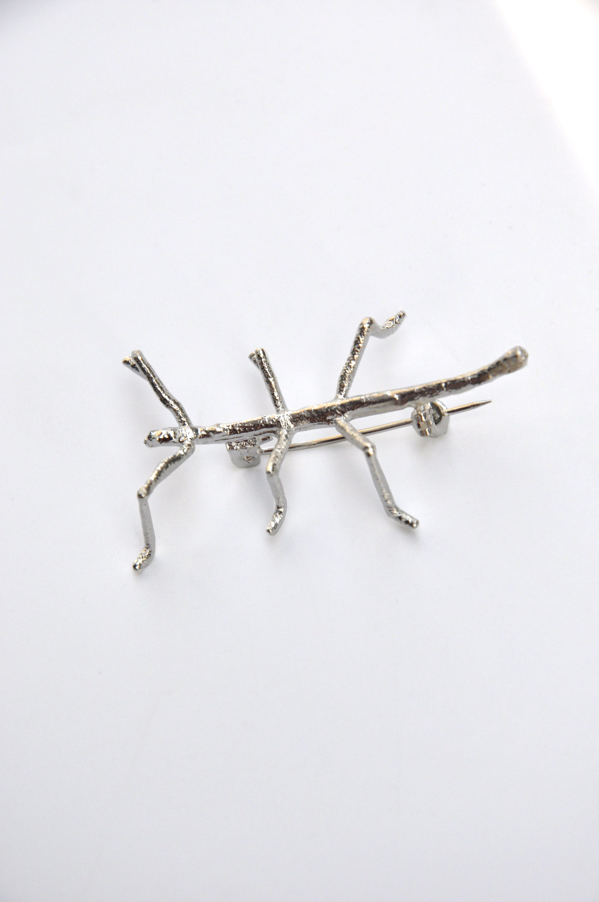 Side profile of the silver stick insect brooch on a clean white background, emphasizing its natural form.