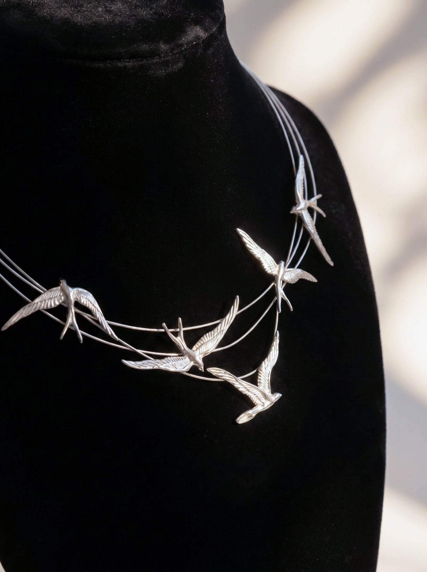 Close-up of Swallow Arch Necklace in sterling silver displayed on black velvet bust, showing sculpted swallows mid-flight forming a graceful arc around the neckline.