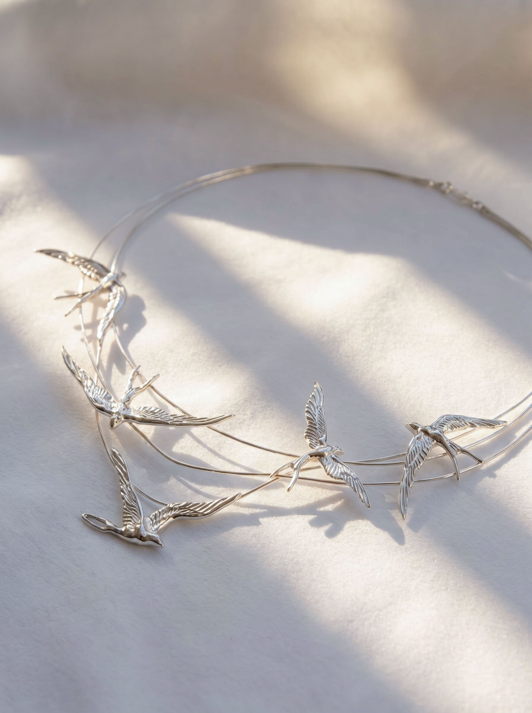 Swallow Arch Necklace photographed flat under soft light, revealing delicate alignment of sculpted swallows in motion.