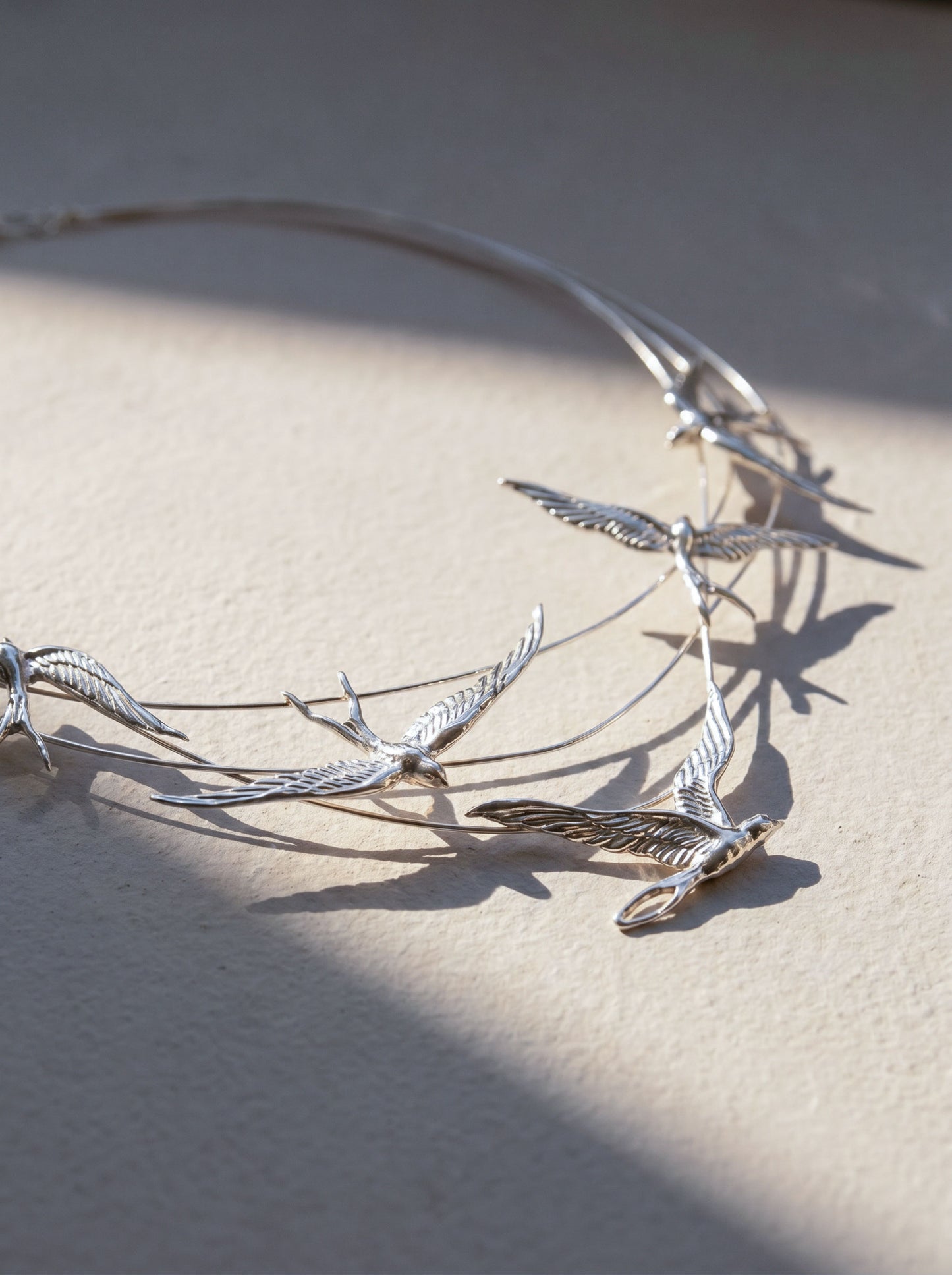 Swallow Arch Necklace photographed at an angle, with shadows emphasizing the dimensional sculptural design.