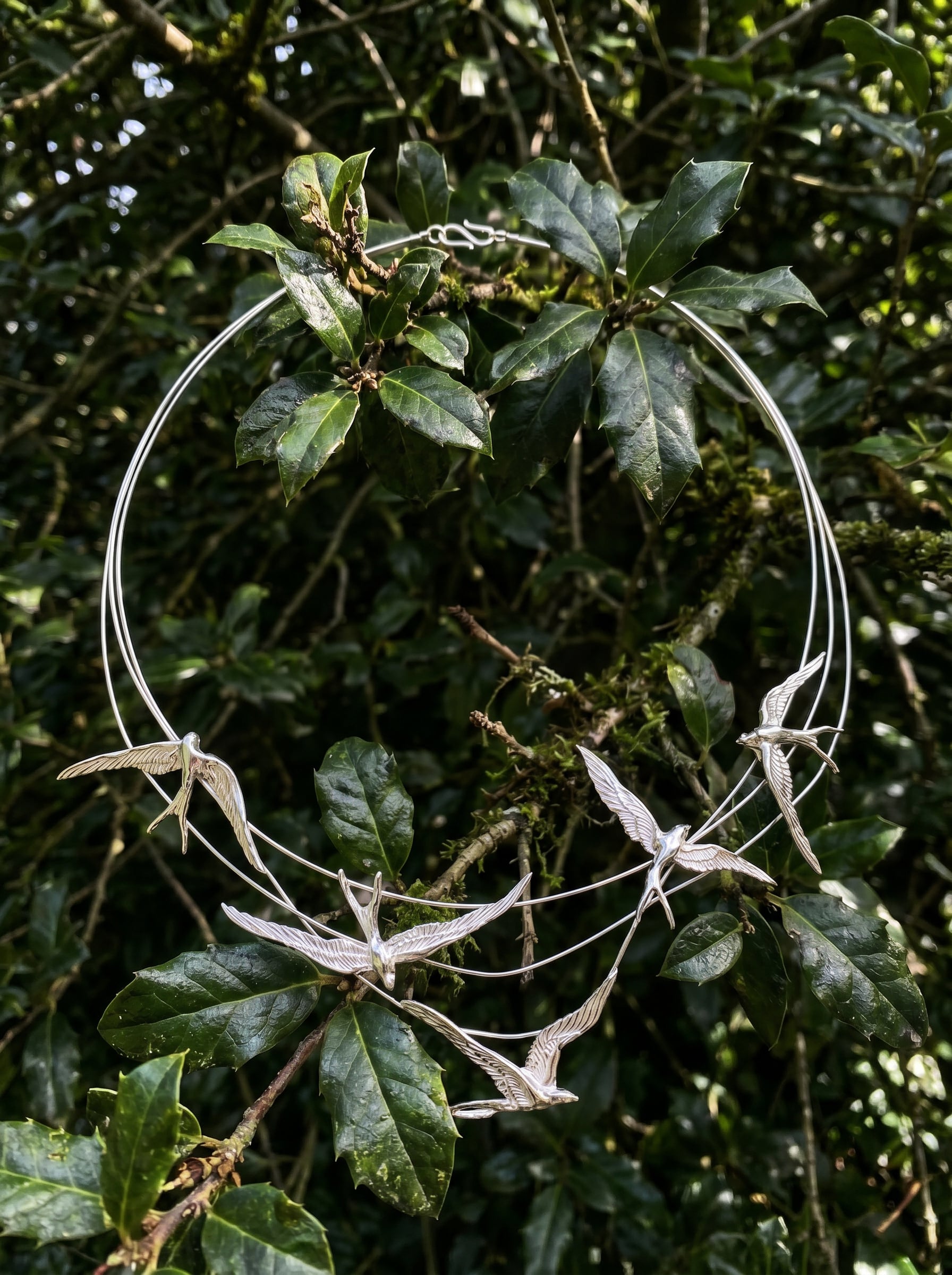 Swallow Arch Necklace photographed against green foliage, emphasizing natural inspiration and airy sculptural form.