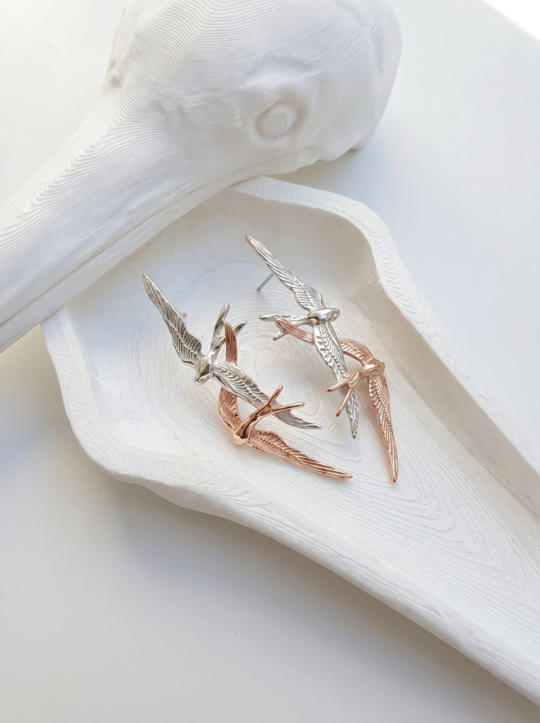 Swallow Flight Stud Earrings displayed on white tray, highlighting fine detailing and contrasting silver and rose‑gold tones.