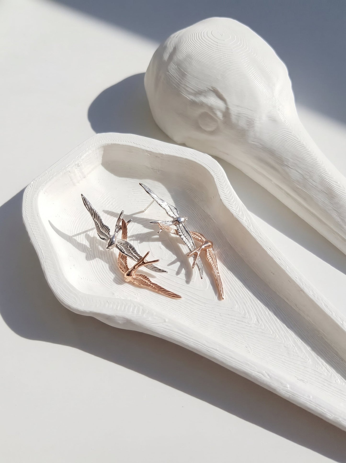 Swallow Flight Stud Earrings displayed on white tray, showing delicate asymmetry and mirror‑polished surfaces.