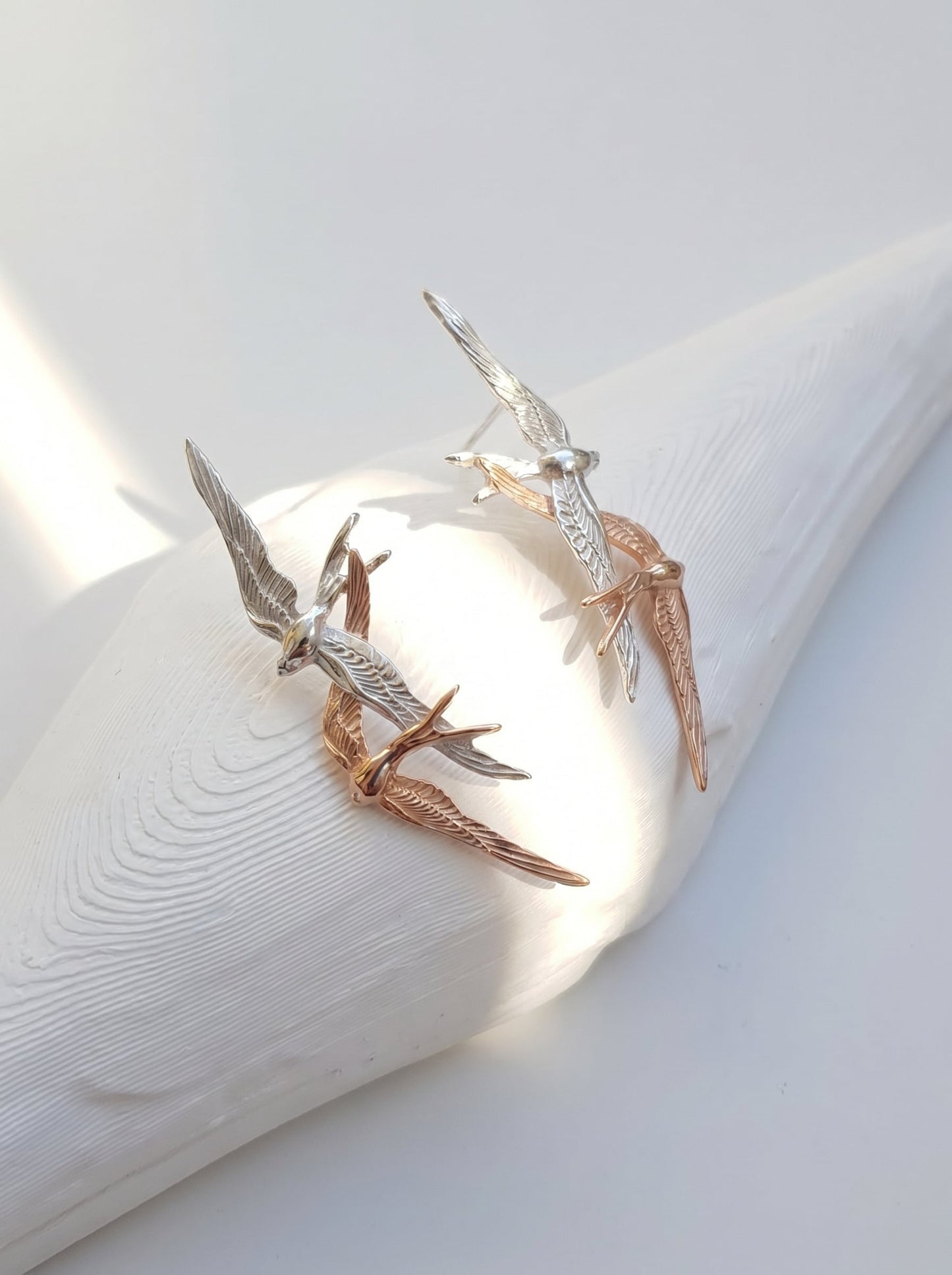 Swallow Flight Stud Earrings photographed at an angle, revealing fine feather engravings and warm rose‑gold highlights.