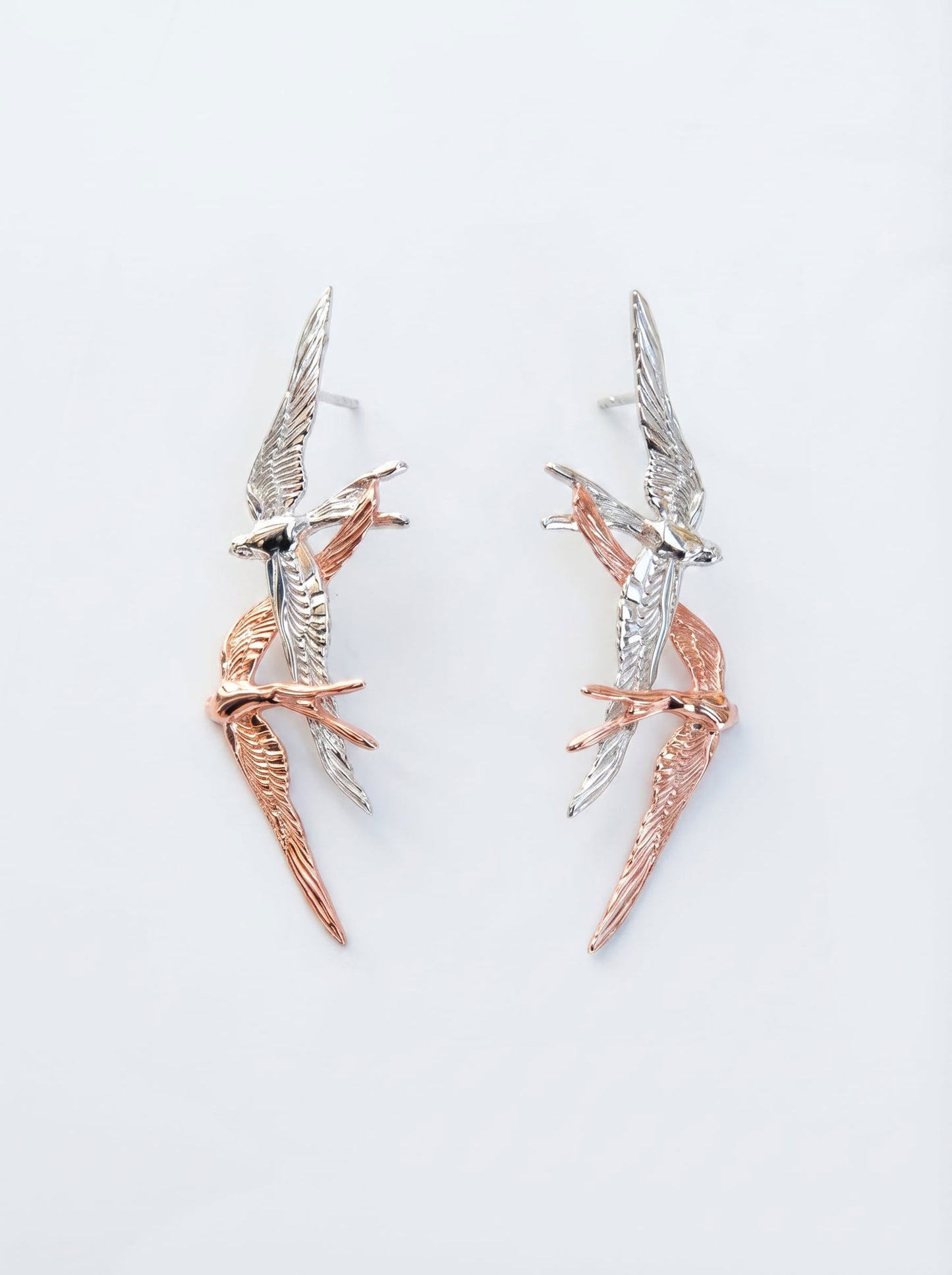 Swallow Flight Stud Earrings photographed flat, showing mirrored birds and refined craftsmanship in silver and rose‑gold finishes.