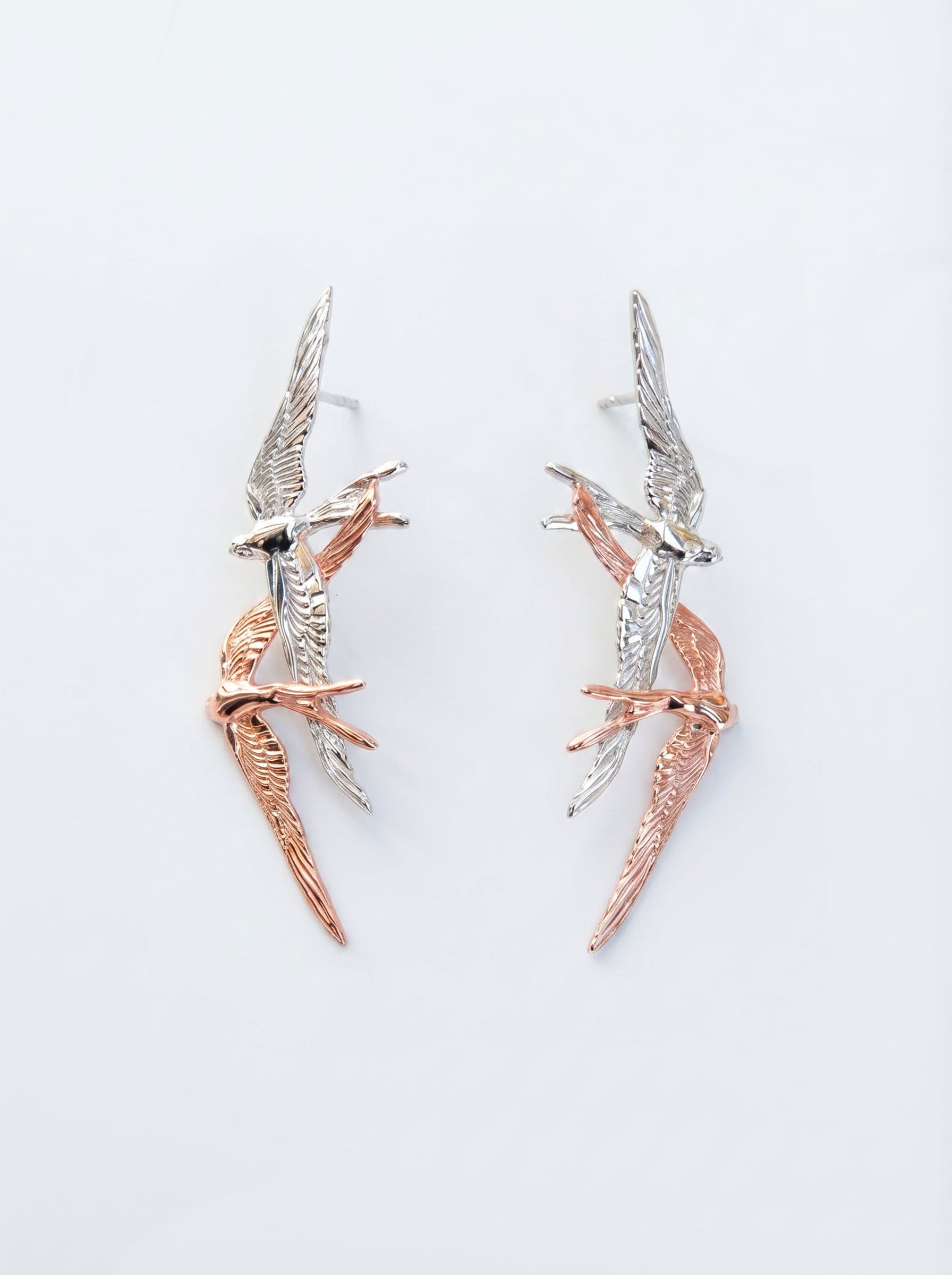 Swallow Flight Stud Earrings photographed flat, showing mirrored birds and refined craftsmanship in silver and rose‑gold finishes.