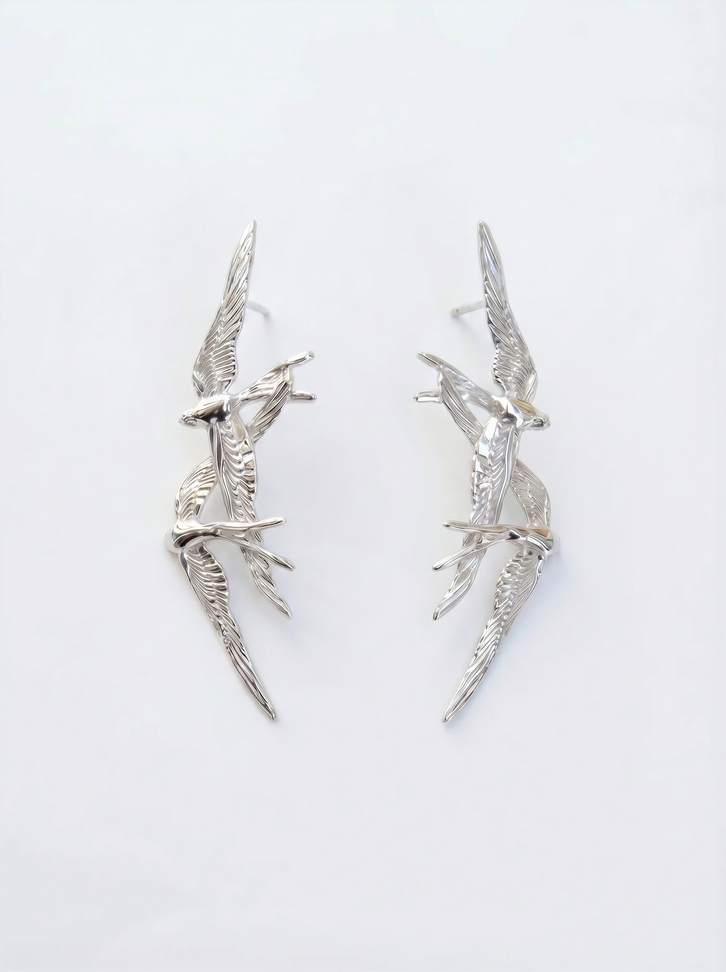 Swallow Flight Stud Earrings in full sterling silver, photographed flat on white surface, emphasizing polished contours and engraved wing detail.