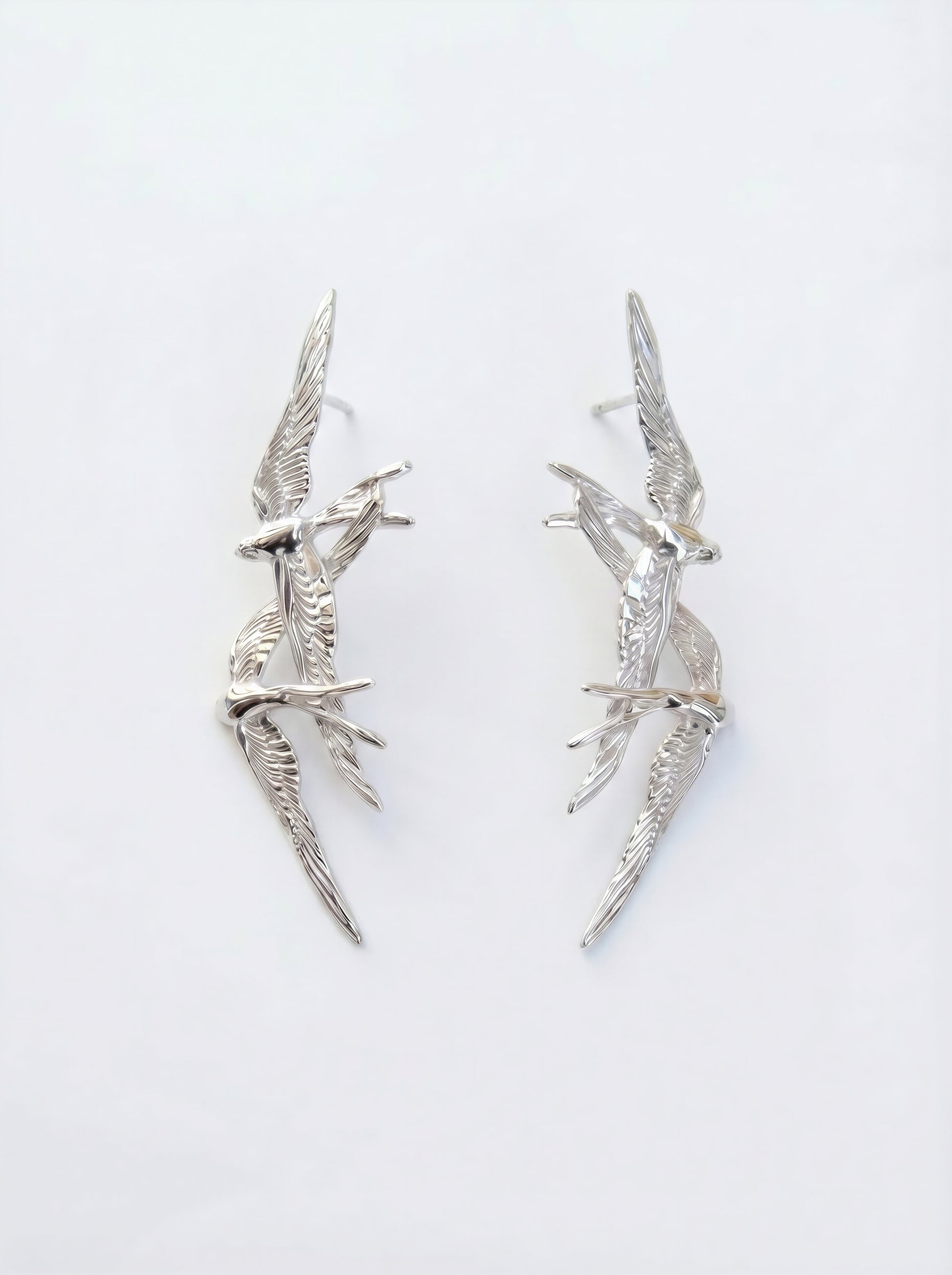 Swallow Flight Stud Earrings in full sterling silver, photographed flat on white surface, emphasizing polished contours and engraved wing detail.