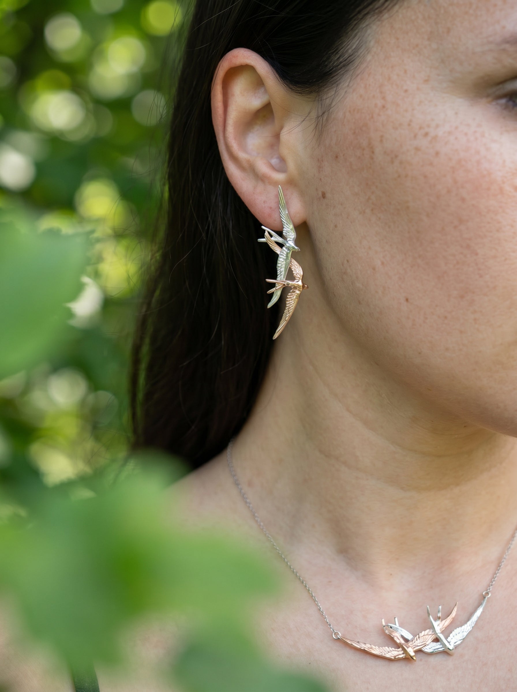 Close‑up of Swallow Flight Stud Earrings worn outdoors, capturing delicate wing engravings and interplay of silver and rose‑gold hues.